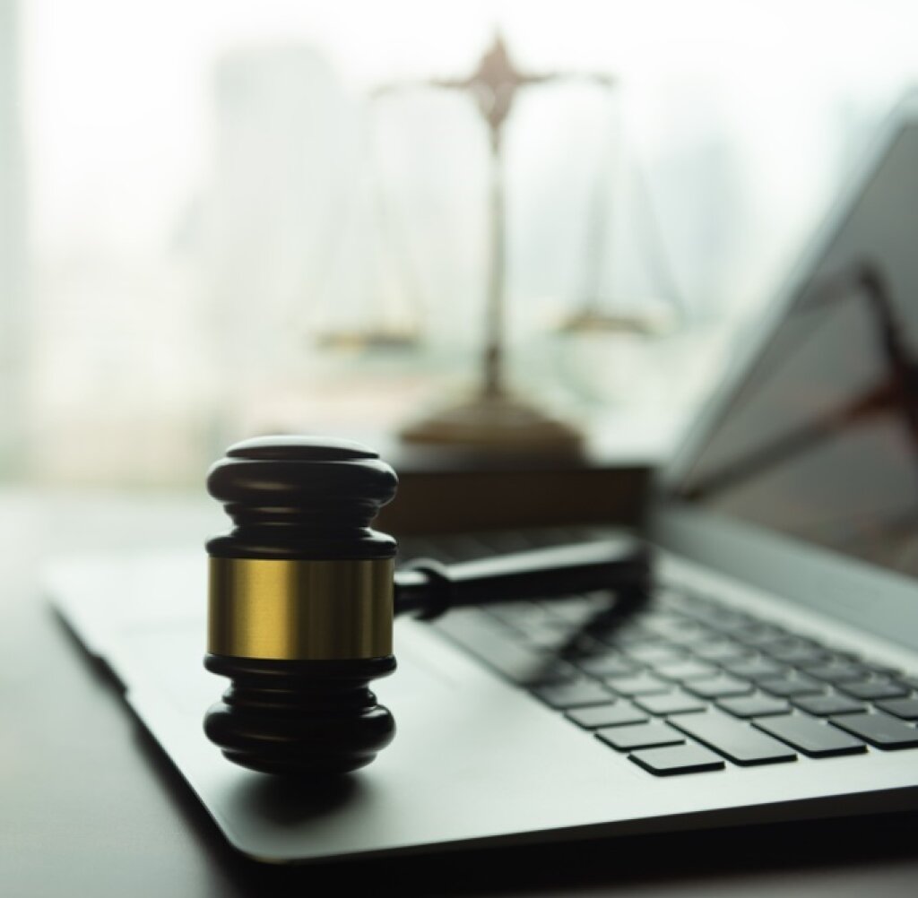 Laptop with a gavel on it, with balance scales in the background.