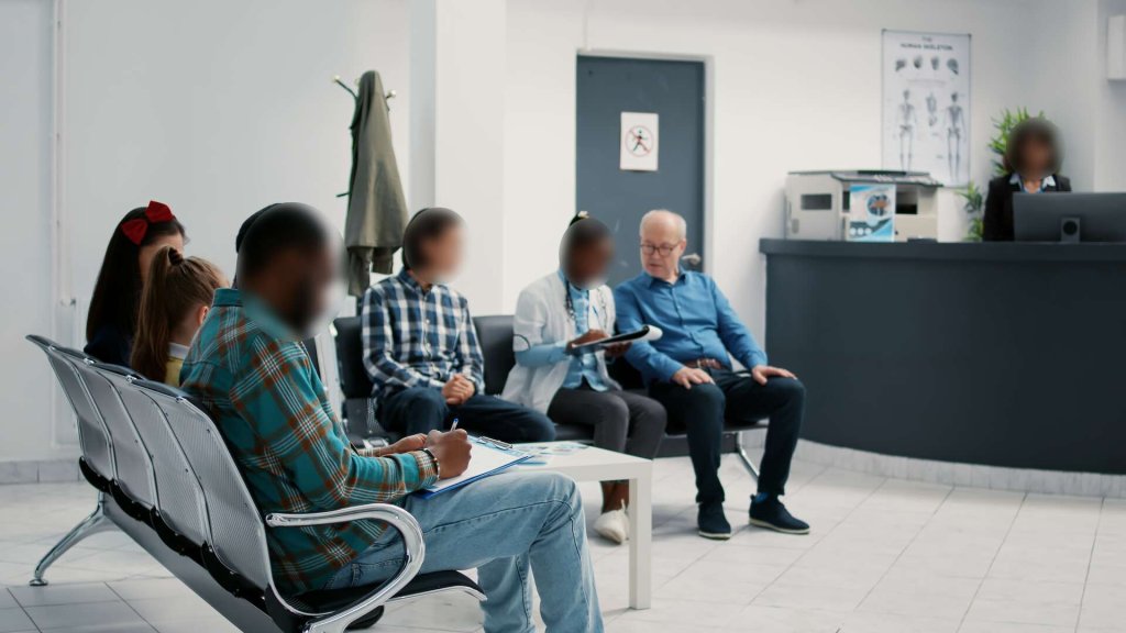People sat in a medical waiting room – all except one face is redacted.