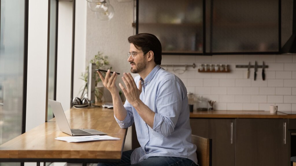 Person at their laptop talking into their mobile phone.