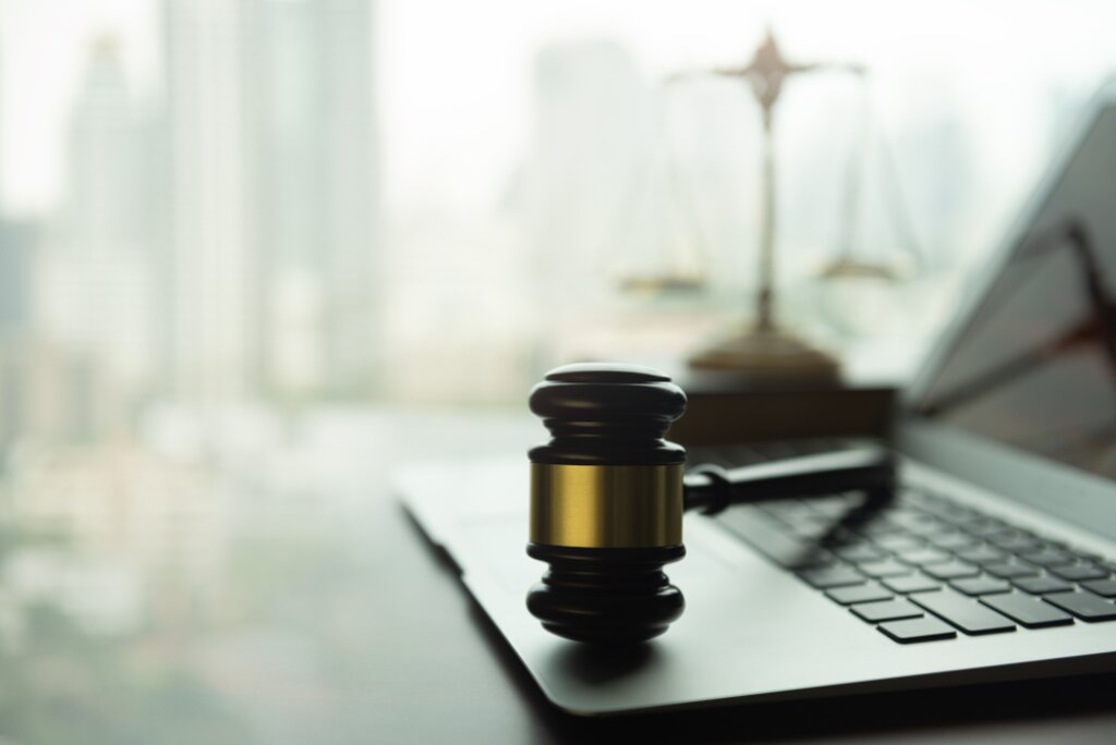 Laptop with a gavel on it, with balance scales in the background.